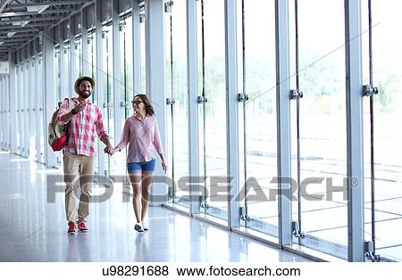 Stock Photo - Full-length of couple holding hands while walking at covered passage. Fotosearch