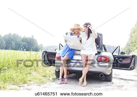 Full length of female friends reading map while leaning on convertible in countryside View Large Photo Image Stock Image - Full length of female friends reading map while leaning on convertible in countryside. Fotosearch