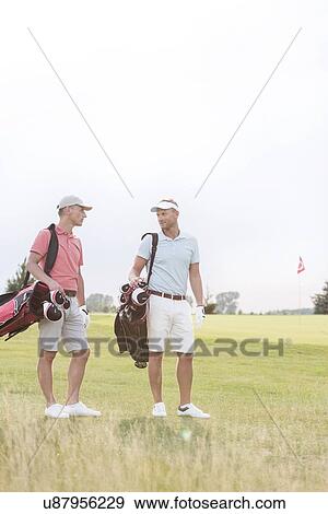 Stock Photo - Full-length of men conversing at golf course against clear sky. Fotosearch