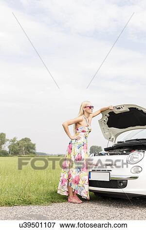 Full-length of tensed woman standing by broken down car on country road View Large Photo Image Stock Photo - Full-length of tensed woman standing by broken down car on country road. Fotosearch