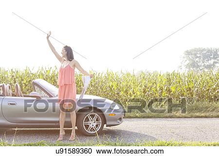 Stock Image - Full length of woman gesturing while holding map by convertible against clear sky. Fotosearch