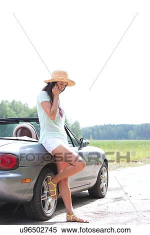 Full-length of woman using cell phone while leaning on convertible at countryside View Large Photo Image Stock Photography - Full-length of woman using cell phone while leaning on convertible at countryside. Fotosearch