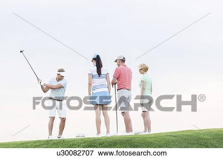 Group of friends looking at man playing golf against clear sky View Large Photo Image Stock Photo - Group of friends looking at man playing golf against clear sky. Fotosearch