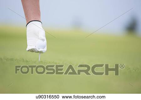 Stock Image - Hand holding ball and tee at golf course. Fotosearch