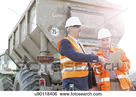 Stock Photograph - Happy architects discussing over clipboard by construction truck. Fotosearch