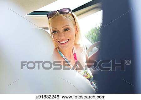 Stock Photography - Happy beautiful woman looking back while driving car. Fotosearch