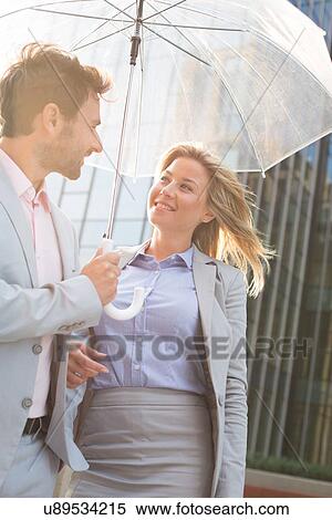 Stock Photography - Happy business couple conversing under umbrella outdoors. Fotosearch