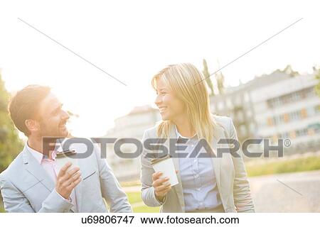 Stock Photo - Happy business couple conversing while holding disposable cups in city. Fotosearch