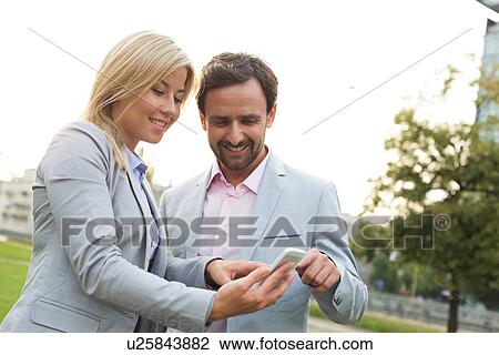 Stock Image - Happy business couple using smart phone at park. Fotosearch