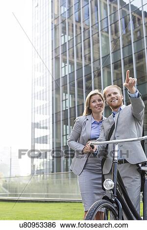 Stock Photograph - Happy businessman showing something to businesswoman in city. Fotosearch