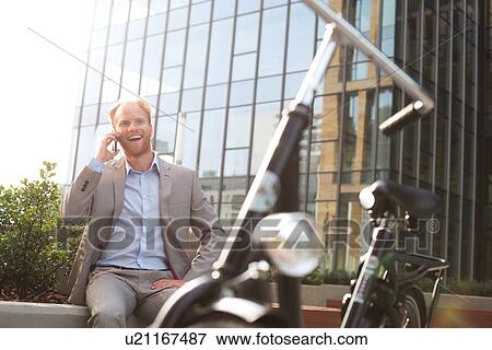 Stock Photo - Happy businessman using mobile phone outside office building. Fotosearch