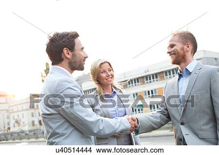 Picture - Happy businessmen shaking hands in city against clear sky. Fotosearch