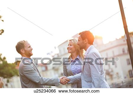 Happy businessmen shaking hands in city against clear sky View Large Photo Image Stock Photograph - Happy businessmen shaking hands in city against clear sky. Fotosearch