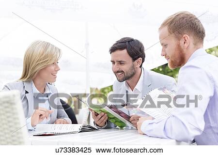 Stock Photography - Happy businesspeople reading menu at sidewalk cafe. Fotosearch