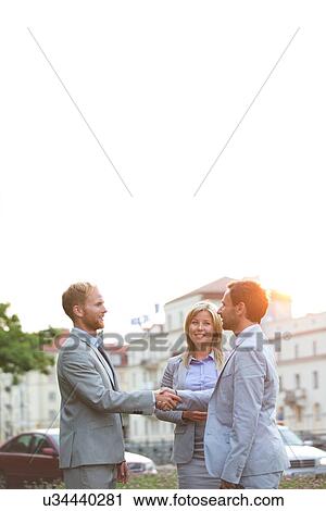 Happy businesspeople shaking hands in city against clear sky View Large Photo Image Stock Image - Happy businesspeople shaking hands in city against clear sky. Fotosearch