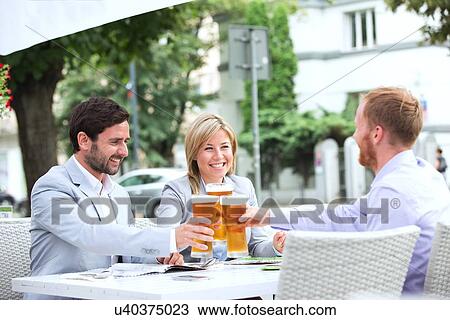 Stock Image - Happy businesspeople toasting beer glasses at outdoor restaurant. Fotosearch