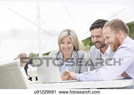 Happy businesspeople using laptop at sidewalk cafe View Large Photo Image Stock Image - Happy businesspeople using laptop at sidewalk cafe. Fotosearch