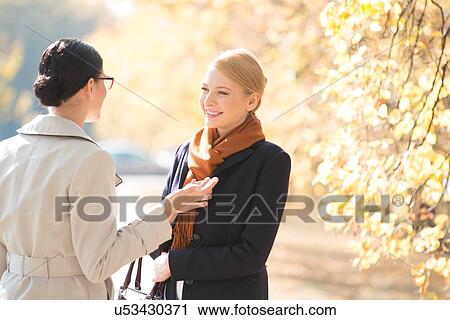 Happy businesswoman conversing with colleague at park on sunny day View Large Photo Image Stock Image - Happy businesswoman conversing with colleague at park on sunny day. Fotosearch