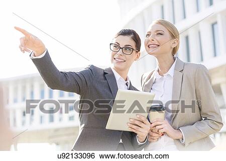 Stock Photograph - Happy businesswoman showing something to colleague while using tablet PC. Fotosearch