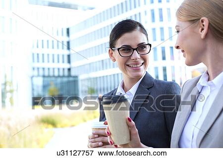 Happy businesswomen conversing while holding disposable cups outdoors View Large Photo Image Stock Photo - Happy businesswomen conversing while holding disposable cups outdoors. Fotosearch