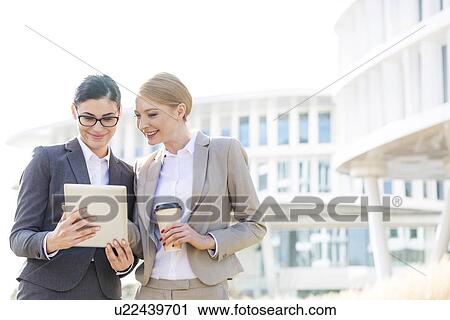 Happy businesswomen using digital tablet outside office building View Large Photo Image Stock Image - Happy businesswomen using digital tablet outside office building. Fotosearch