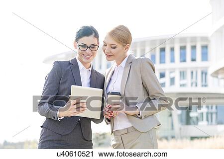 Stock Image - Happy businesswomen using tablet PC outside office building. Fotosearch