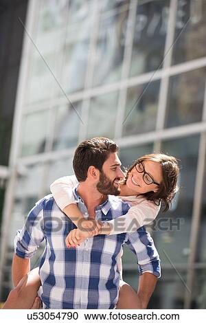 Happy couple looking at each other while enjoying piggyback ride in city View Large Photo Image Stock Image - Happy couple looking at each other while enjoying piggyback ride in city. Fotosearch