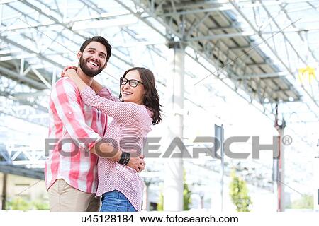 Picture - Happy couple looking away while embracing outside building. Fotosearch