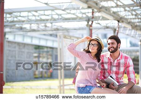 Happy couple looking away while sitting on bench under shade View Large Photo Image Stock Photograph - Happy couple looking away while sitting on bench under shade. Fotosearch