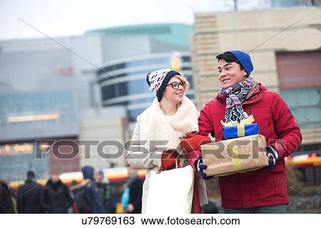 Stock Image - Happy couple with gifts and shopping bags walking in city during winter. Fotosearch