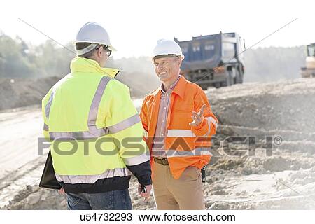 Stock Image - Happy engineer talking to colleague at construction site on sunny day. Fotosearch