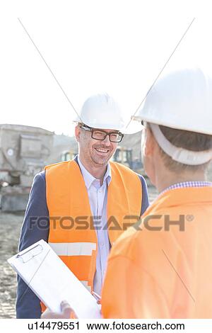 Stock Image - Happy engineers discussing at construction site against clear sky. Fotosearch
