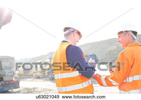Happy engineers discussing over clipboard at construction site against clear sky View Large Photo Image Stock Photo - Happy engineers discussing over clipboard at construction site against clear sky. Fotosearch