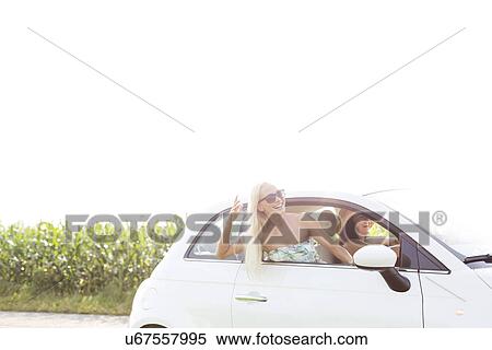 Happy female friends enjoying in car against clear sky View Large Photo Image Stock Photography - Happy female friends enjoying in car against clear sky. Fotosearch