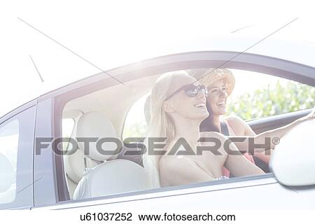 Happy female friends enjoying road trip in car on sunny day View Large Photo Image Stock Image - Happy female friends enjoying road trip in car on sunny day. Fotosearch