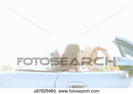 Stock Photography - Happy female friends enjoying road trip in convertible on sunny day. Fotosearch