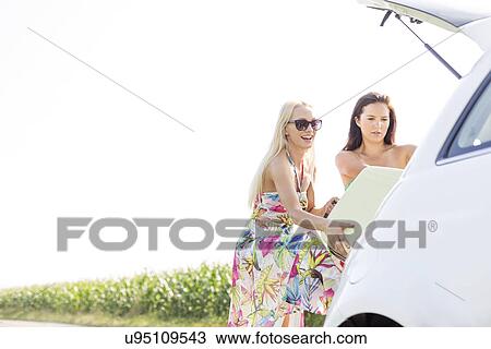 Happy female friends loading luggage in car trunk against clear sky View Large Photo Image Stock Image - Happy female friends loading luggage in car trunk against clear sky. Fotosearch