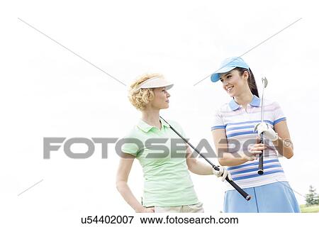 Happy female golfers looking at each other against clear sky View Large Photo Image Stock Photo - Happy female golfers looking at each other against clear sky. Fotosearch