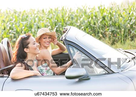 Stock Image - Happy friends enjoying road trip in convertible. Fotosearch