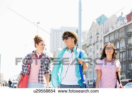 Picture - Happy friends talking while walking in city. Fotosearch