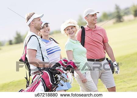 Stock Image - Happy friends walking at golf course. Fotosearch