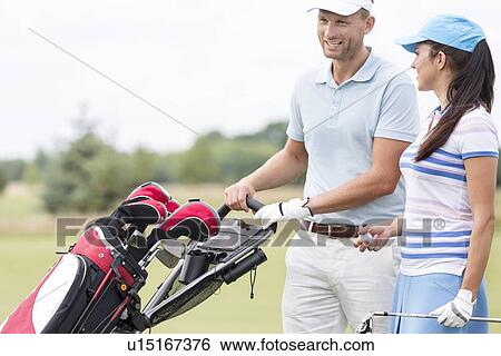 Stock Photograph - Happy friends with bag talking at golf course. Fotosearch