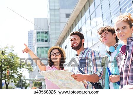 Happy friends with road map with woman pointing away in city View Large Photo Image Stock Photograph - Happy friends with road map with woman pointing away in city. Fotosearch