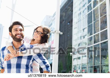 Stock Photo - Happy man giving piggyback ride to woman in city. Fotosearch