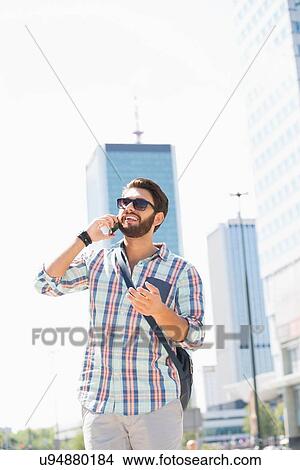 Picture - Happy man looking away while using cell phone in city. Fotosearch