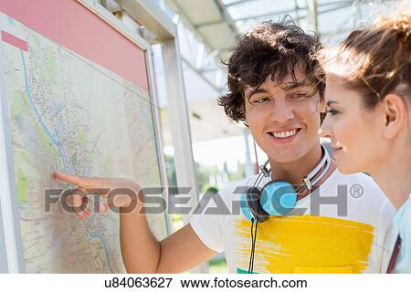 Stock Photo - Happy man showing places on map to woman outdoors. Fotosearch