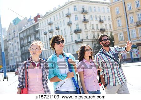 Stock Photo - Happy man showing something to male and female friends on city street. Fotosearch