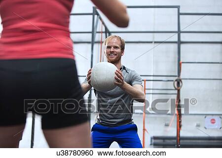 Happy man throwing medicine ball towards woman in crossfit gym View Large Photo Image Stock Image - Happy man throwing medicine ball towards woman in crossfit gym. Fotosearch