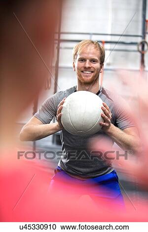 Stock Image - Happy man throwing medicine ball towards woman in crossfit gym. Fotosearch