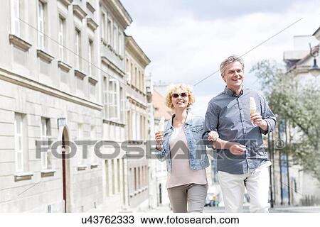 Happy middle-aged couple holding ice cream cones while walking in city View Large Photo Image Stock Image - Happy middle-aged couple holding ice cream cones while walking in city. Fotosearch
